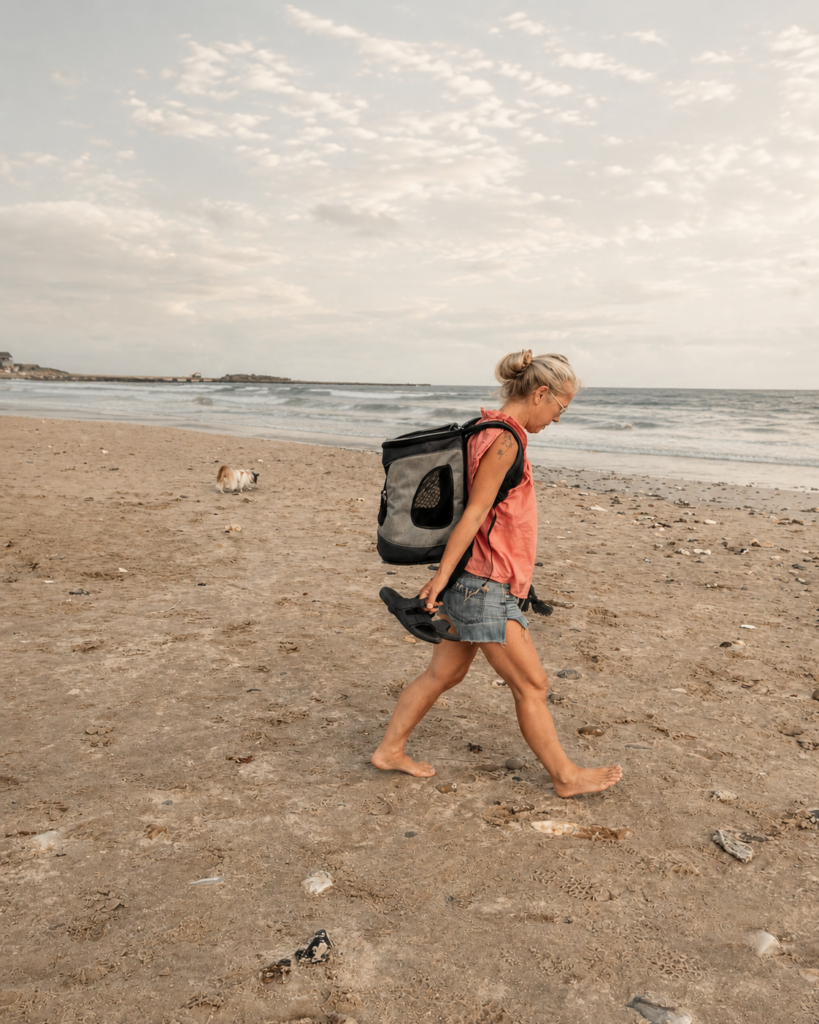 Ingrid loopt blootsvoets over het strand met haar hond, met de zee op de achtergrond.